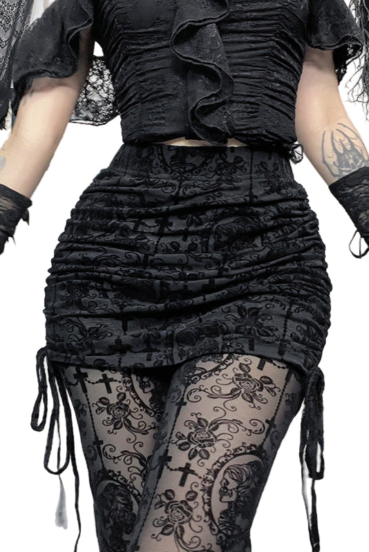 Person wearing a black ruffled top and skirt with sheer tights featuring skull designs, standing in a Halloween-themed room.