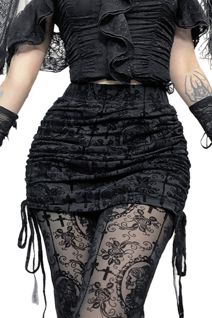 Person wearing a black ruffled top and skirt with sheer tights featuring skull designs, standing in a Halloween-themed room.