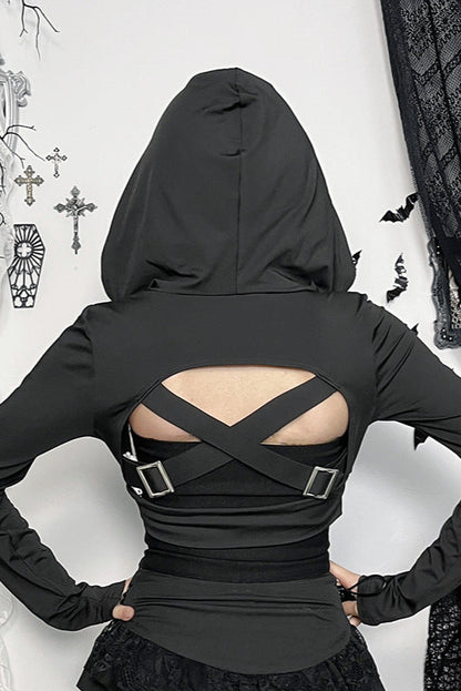Person wearing a black hooded top with cut-out design, standing against a decorative wall.