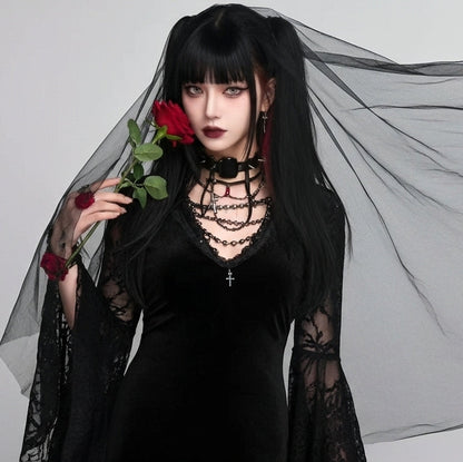 Person in a black dress with sheer sleeves holding a red rose against a gray background